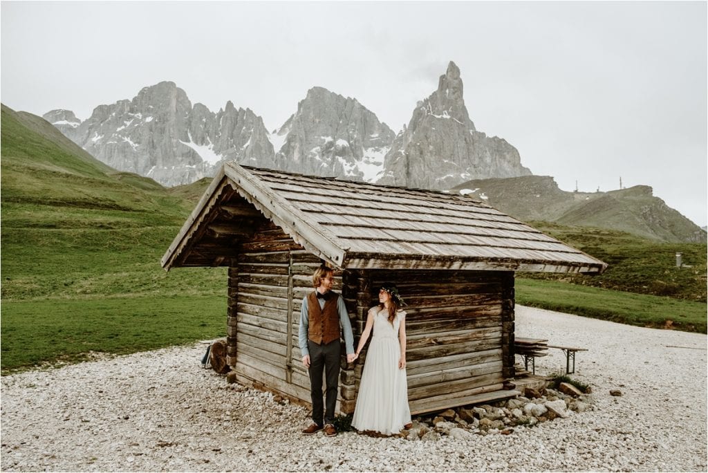 The couple hides under the roof of a wooden hut in the Dolomites to escape the rain on their wedding day. By Wild Connections Photography