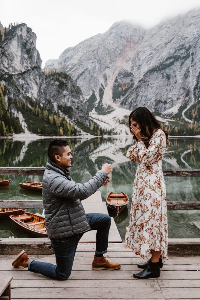 Man on one knee proposing to his girlfriend in front of Lago di Braies in the Dolomites in Italy on the stepy of the boathouse