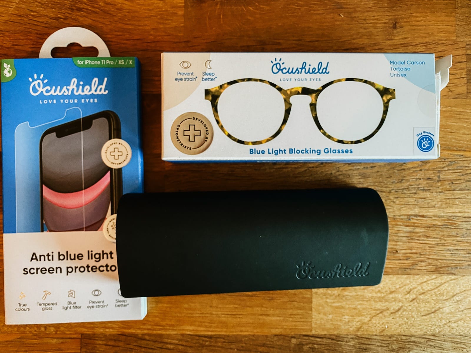 A photo showing blue light blocking glasses and a smartphone screen protector from Ocushield lying on a wooden table