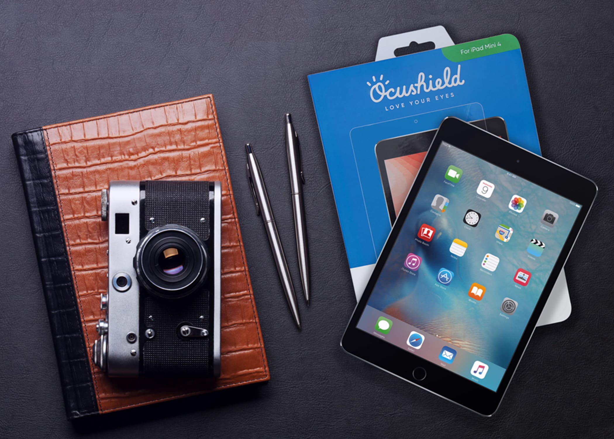 Photo of a camera on top of a leather notebook next to an Ocushield blue light tablet screen protector and the box from Ocushield