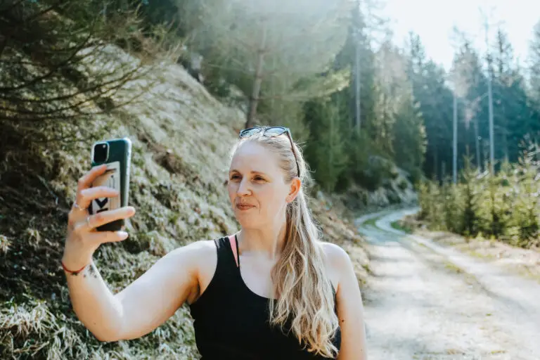 Photo of a woman holding up a phone. She is recording a selfie video.
